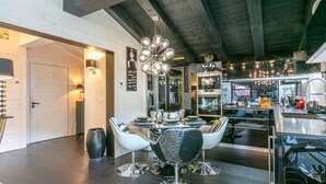 Een moderne keuken met roestvrijstalen apparatuur, een eethoek met moderne stoelen en een plafond met zichtbare balken.