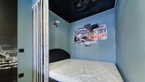 Une chambre à coucher avec un lit, une tête de lit, une lampe fixée au mur et une fresque représentant un paysage urbain.