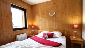 Ett sovrum med träpanel på väggarna, en säng, två sängbord, ett fönster och en dekorativ krans som hänger på väggen.