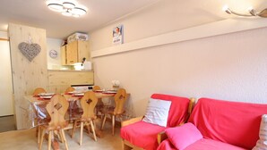 Ett mysigt rum med ett matbord, trästolar, en röd soffa och ett köksområde i bakgrunden.