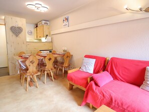 A cozy room with a dining table, wooden chairs, a red sofa, and a kitchen area in the background.
