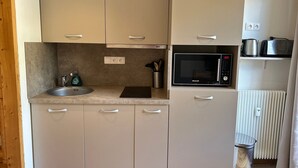 Cocina compacta con lavamanos, encimera, microondas y radiador.