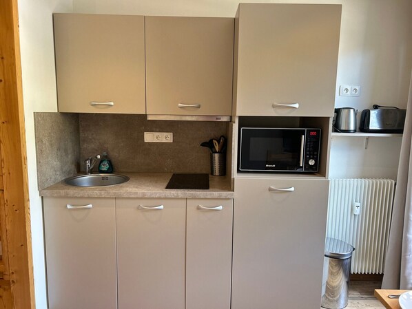 A compact kitchen with a sink, countertop, microwave, and a radiator.