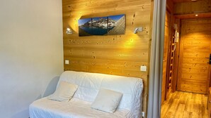 Una habitación acogedora con cabecera de madera, cama con ropa de cama blanca, un cuadro de un paisaje montañoso y una puerta de madera.