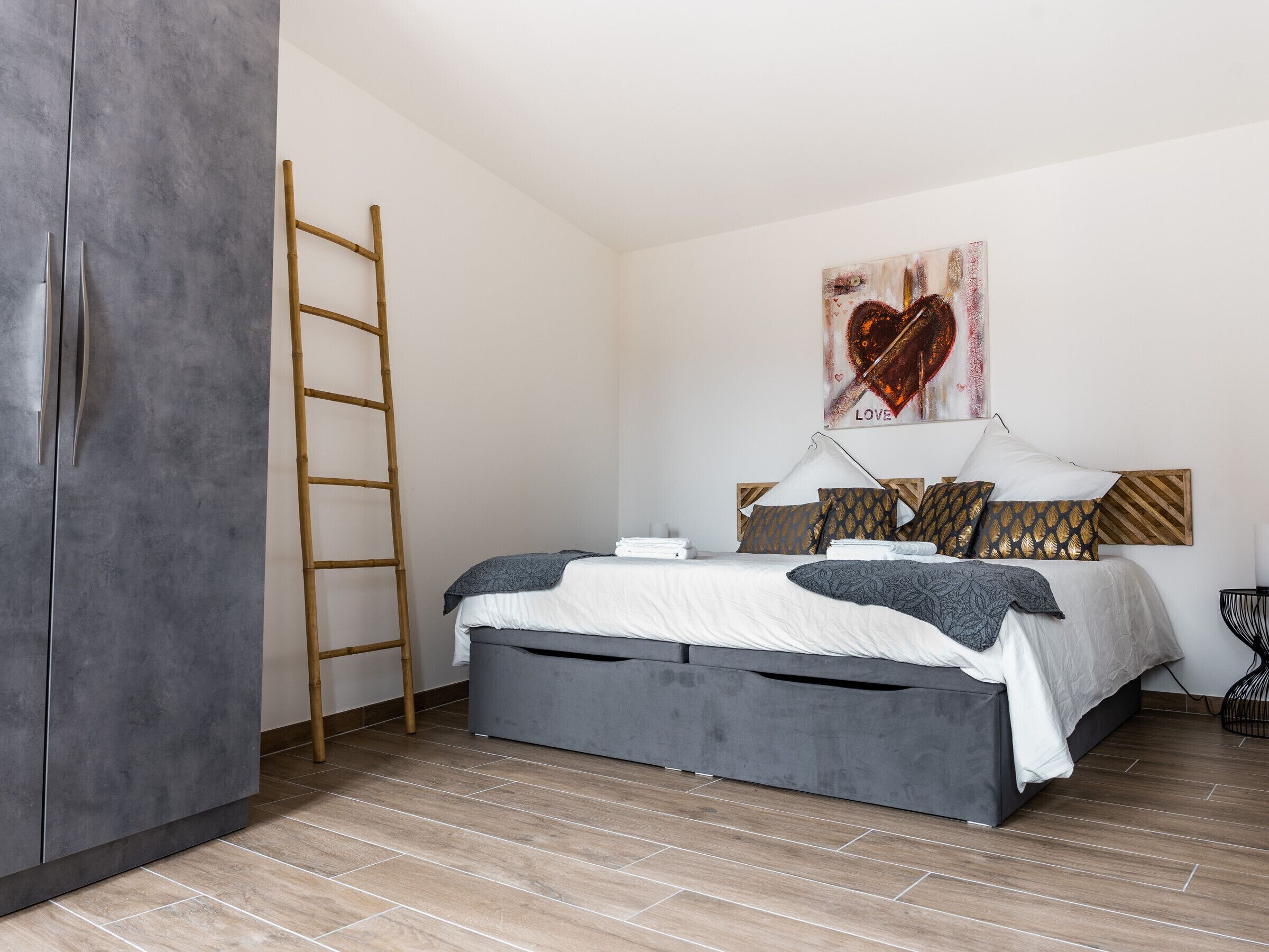 A bedroom with a bed, a ladder, and a painting on the wall.