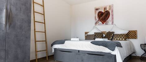 A bedroom with a bed, a ladder, and a painting on the wall.