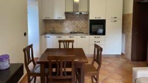 A compact kitchen with white cabinets, a stove, and a dining table with chairs. - HAPPY HOME (Orte)
