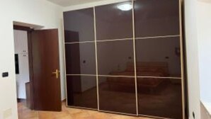 A room with a sliding glass door closet, a wooden door, and a tiled floor. - HAPPY HOME (Orte)
