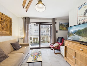 Uma sala de estar com sofá, mesa de centro, televisão e varanda com vista para um edifício.