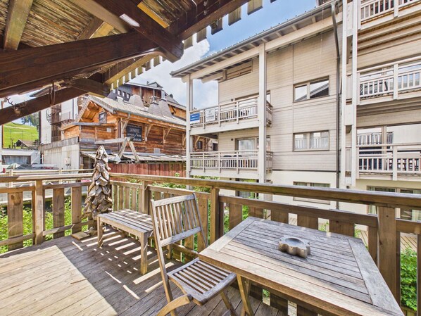 Eine Holzterrasse mit Tisch und StĂŒhlen, mit Blick auf ein GebĂ€ude mit Balkonen und einer Holzfassade.