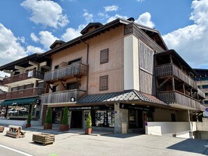 Monikerroksinen rakennus, jossa on puiset parvekkeet, katutasossa sijaitseva liike ja kyltti, jossa lukee: »Nicolas Thibon Immobilier».