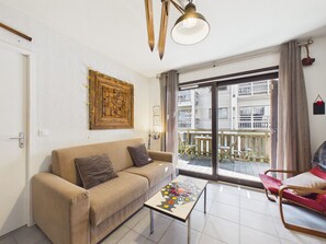 A living room with a sofa, a coffee table, a balcony with a view of buildings, and a hanging light fixture.