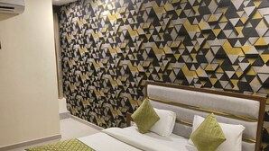 A hotel room with a geometric patterned wall, a bed with white bedding and green accents, and a wooden headboard. - Hotel V R Villa (Vadodara)