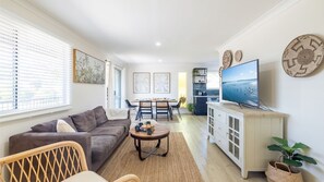 Een moderne woonkamer met een bank, salontafel, televisie, eethoek en keuken.