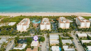 Un hotel frente a la playa con varias edificaciones, una piscina y un estacionamiento.
