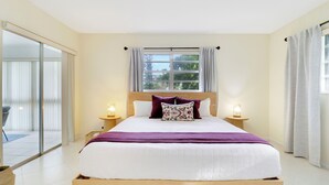 Un dormitorio ordenado con una cama grande, dos mesitas de noche con lámparas, una ventana con cortinas y un ventanal corredizo que da a un balcón.