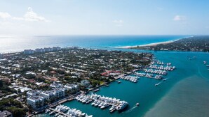 An aerial view of a coastal marina with numerous boats docked, surrounded by residential buildings and a clear view of the ocean.