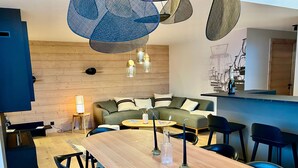 Un soggiorno moderno con pavimento in legno, un divano, un tavolo da pranzo con sedie e lampade pendenti.