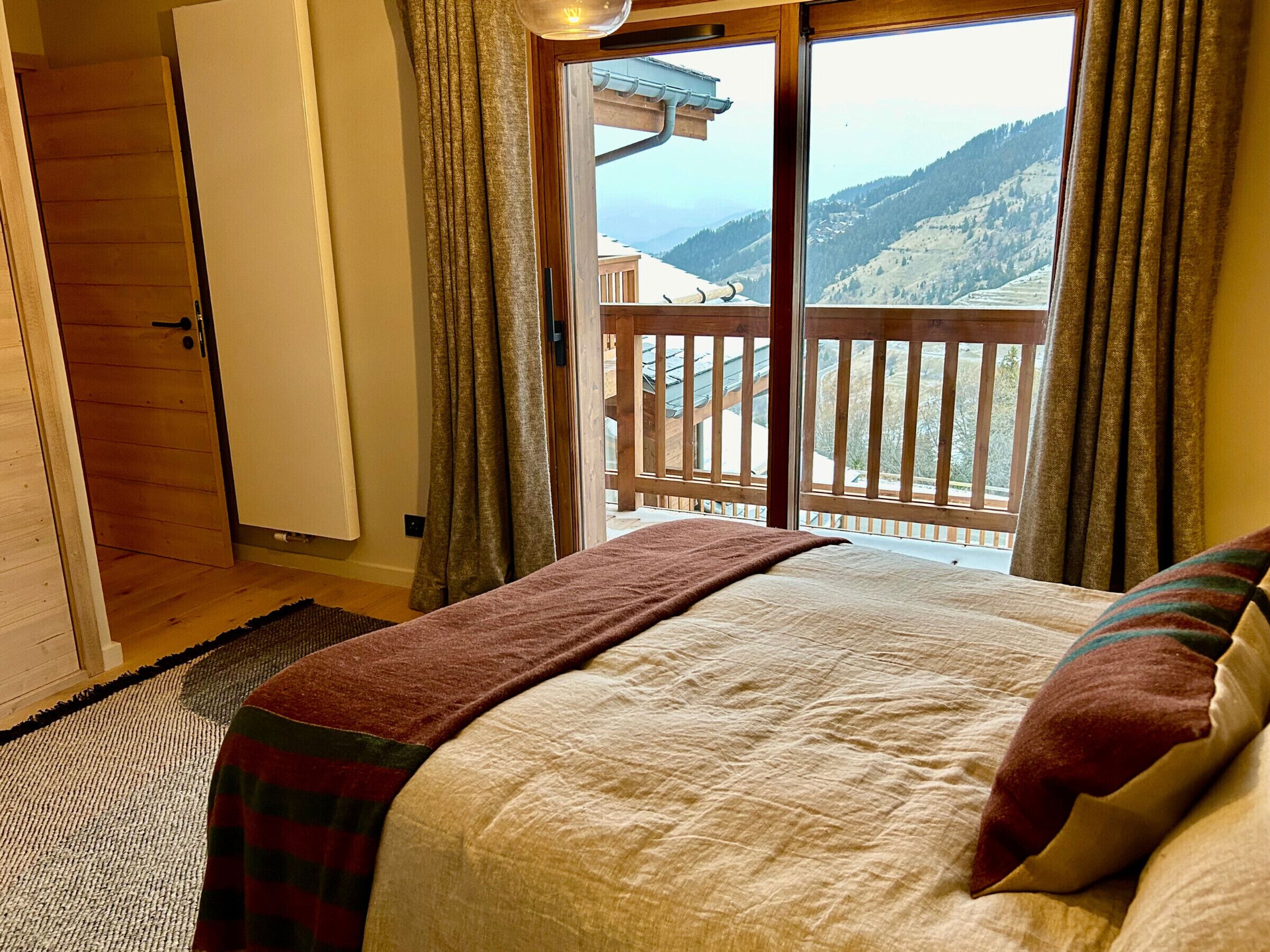 A bedroom with a large bed, a view of a snowy mountain, and a balcony with a wooden railing.