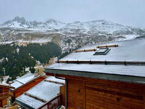Eine Holzhütte mit verschneitem Dach und Blick auf verschneite Berge im Hintergrund.