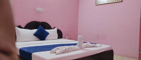 Habitación con paredes rosas, cama con ropa de cama blanca y azul, un cuadro en la pared y un enchufe visible.