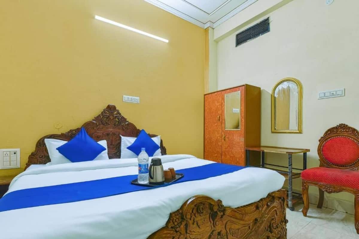 Ein Hotelzimmer mit einem großen Bett, einem Holz-Kopfstück, einem roten Sessel, einer Holzkommode und einem Spiegel an der Wand.