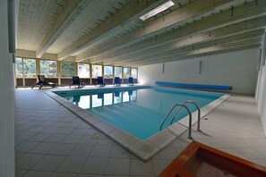 En inomhuspool med kristallklart blått vatten, kaklat golv och flera solstolar.