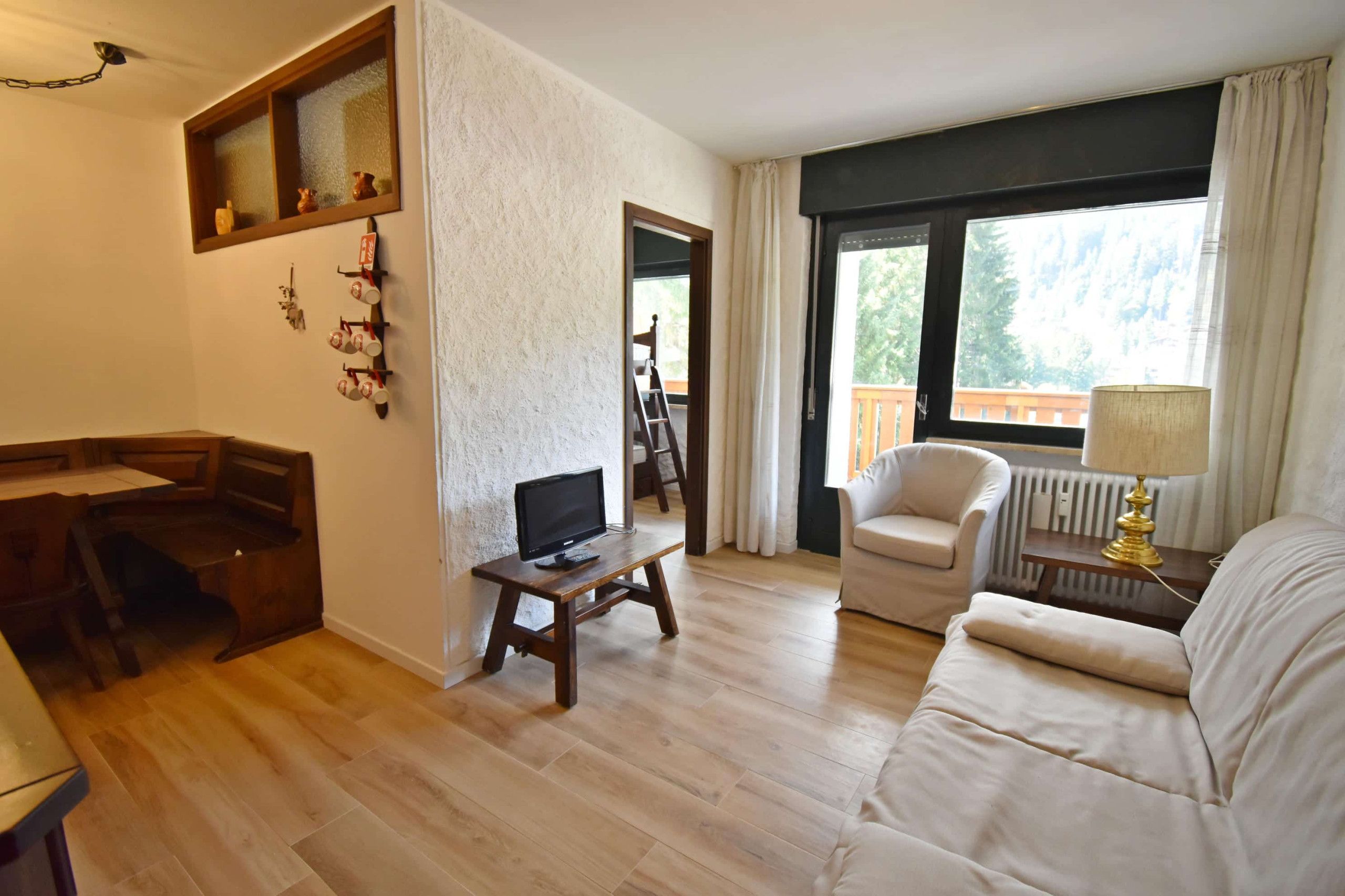Un salon avec un plancher en bois, un canapé, un téléviseur posé sur un meuble, une cheminée et une fenêtre avec des rideaux.