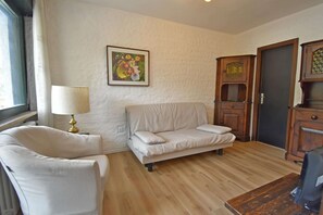 A living room with a beige sofa, a white armchair, a wooden cabinet, and a painting on the wall. - Fevri 109 Appartamento (Madonna di Campiglio)