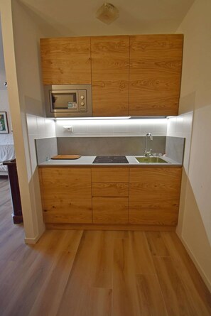A compact kitchen with wooden cabinets, a microwave, a sink, and a stovetop.