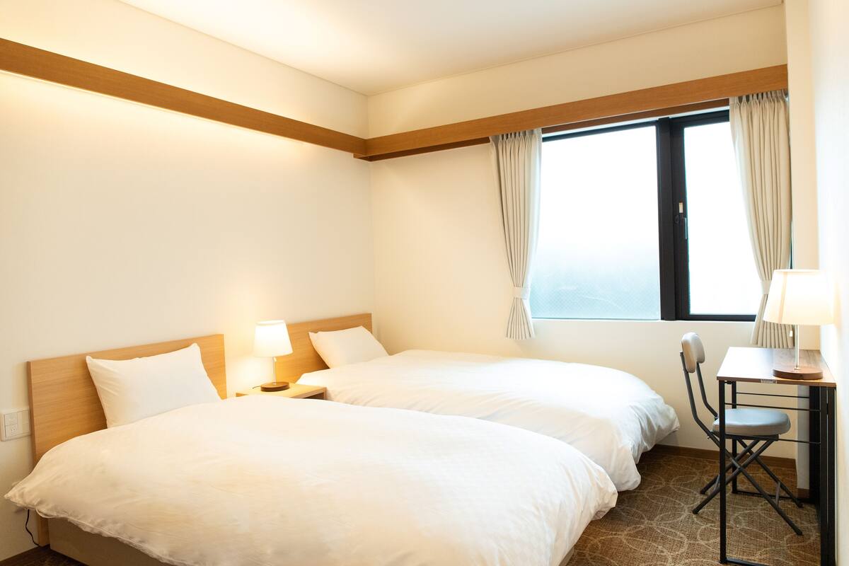 Une chambre d’hôtel avec deux lits, un bureau et une chaise.