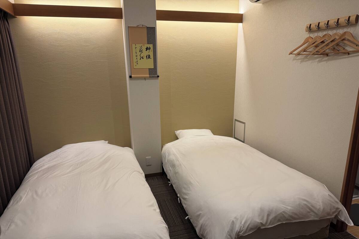 Une chambre d’hôtel avec deux lits simples, un porte-manteau en bois et un mur orné d’un motif texturé.