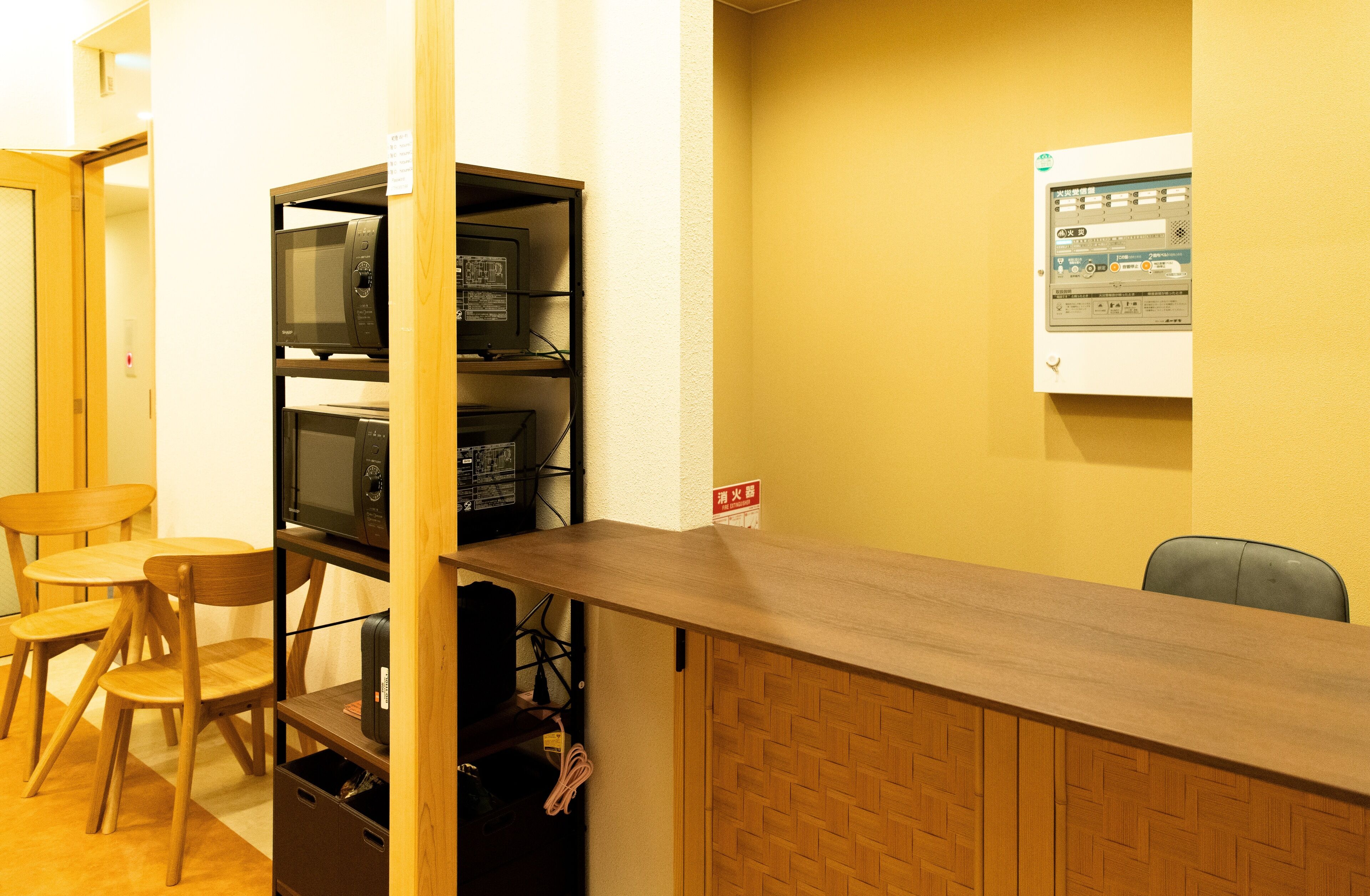 Una habitación con un mostrador de recepción de madera, un microondas y un pequeño rincón de descanso con sillas.