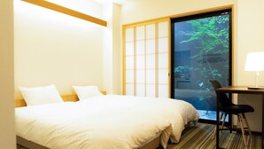 A hotel room with a bed, a desk, and a view of greenery through a sliding door.
