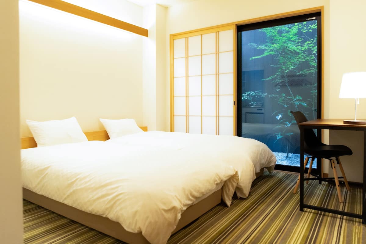 Une chambre d’hôtel avec un lit, un bureau et une vue sur la verdure, accessible par une porte coulissante.