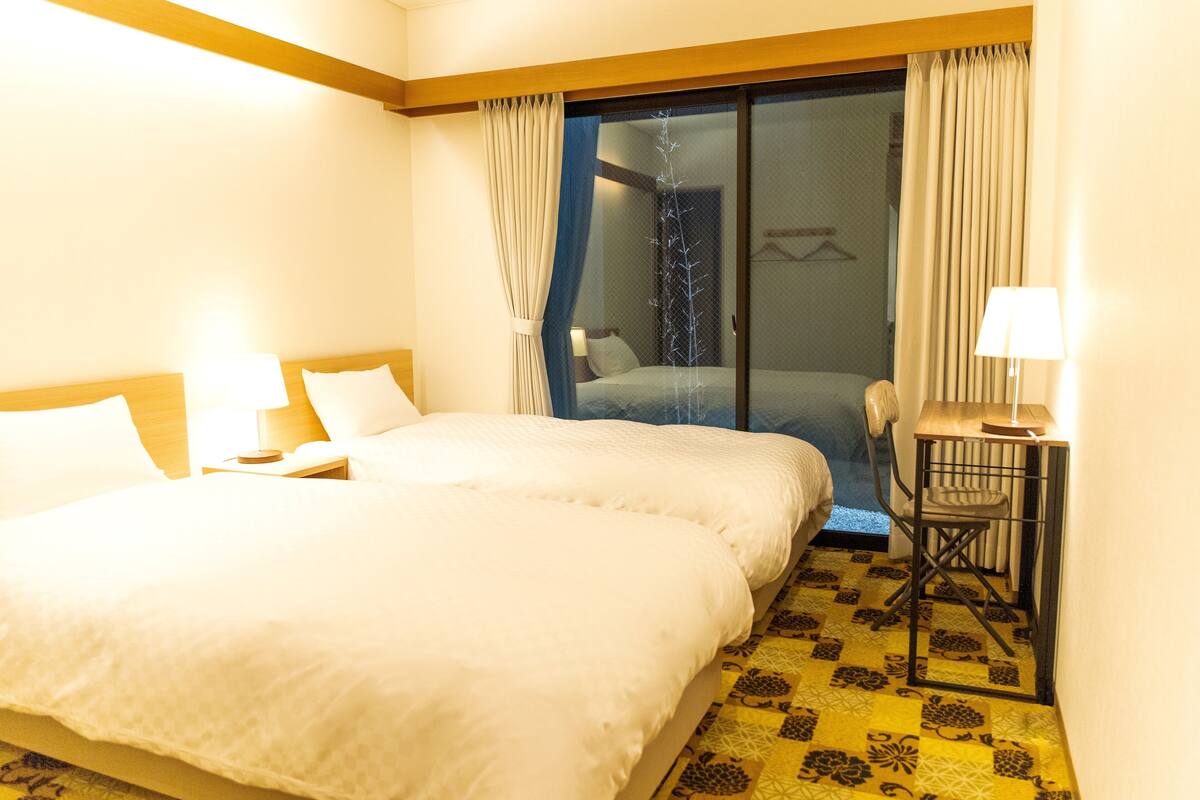 Une chambre d’hôtel avec un grand lit, un bureau avec une chaise et une vue sur l’extérieur, visible à travers une porte vitrée.