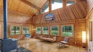 A log cabin interior with a fireplace, large windows, and a painting on the wall. - Elk Meadow (Randle)