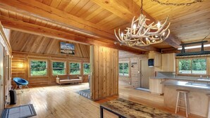 A spacious cabin with a wooden interior, a dining area, and a kitchen. - Elk Meadow (Randle)