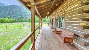 A wooden cabin with a porch, wooden benches, and a view of a forested area. - Elk Meadow (Randle)