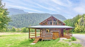 A rustic cabin with a covered porch, wooden deck, and a view of a forested mountain range. - Elk Meadow (Randle)
