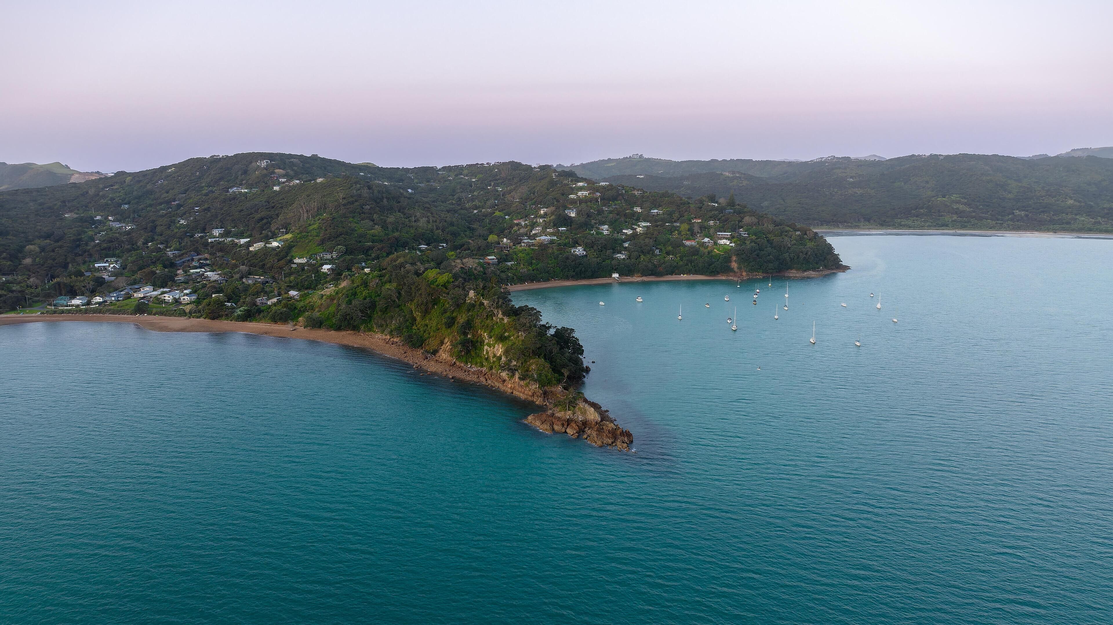 An aerial view of a coastal area with a small island, clear turquoise waters, and several boats.