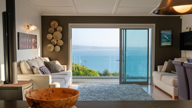 Una sala de estar moderna con un amplio ventanal corredera que da a un balcón con vista al mar.