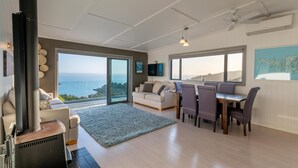 Amplia sala de estar con chimenea, un sofá, una mesa de comedor con sillas y grandes ventanales con vista al mar.