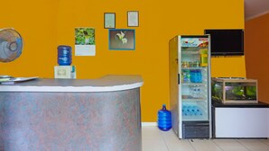 A reception area with a counter, a fan, a water dispenser, a refrigerator stocked with beverages, and a fish tank.