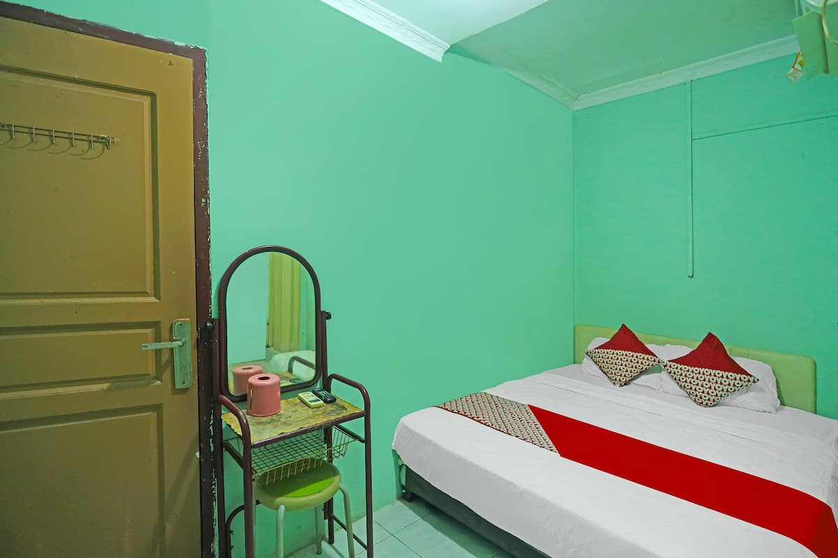 A room with a bed, a desk with a chair, a mirror, and a door.