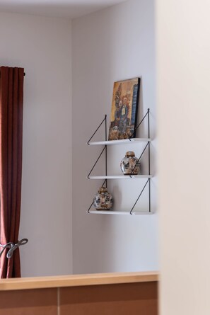 A corner of a room with a white wall, a brown curtain, and a metal shelf with decorative items.