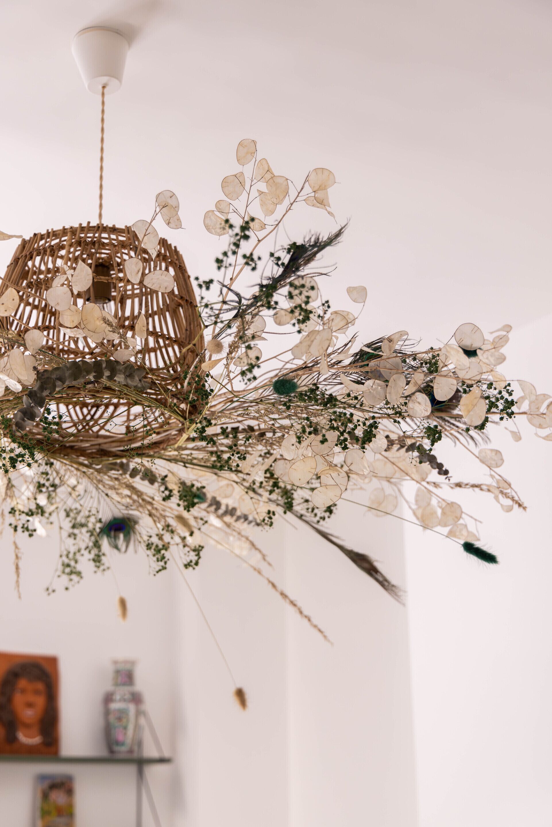 A wicker chandelier with a spherical design, adorned with dried flowers and greenery.