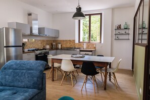 A modern kitchen with a central island, white cabinetry, and a dining area with a blue sofa and chairs. - Domaine Castell de Blés Gîte Canigou (Saint-Genis-des-Fontaines)