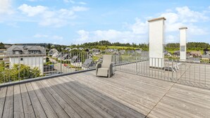 Eine Holzterrasse mit Metallgeländer, mit Blick auf eine Wohngegend mit Häusern und Grünflächen.