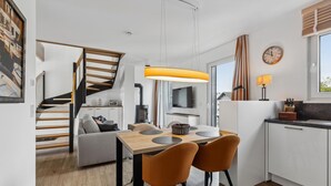 Eine moderne Küche mit Essbereich, einer Holztreppe und einem großen Fenster mit Vorhängen.
